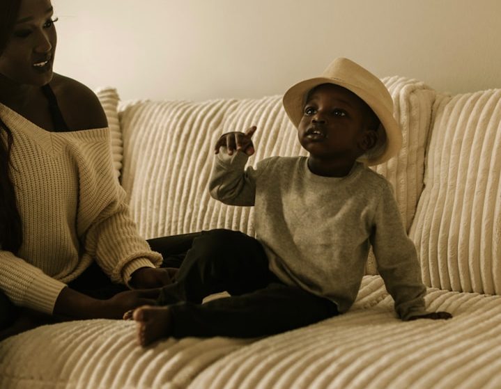 Niño con sombrero sentado en el sofá, conversando con una mujer.