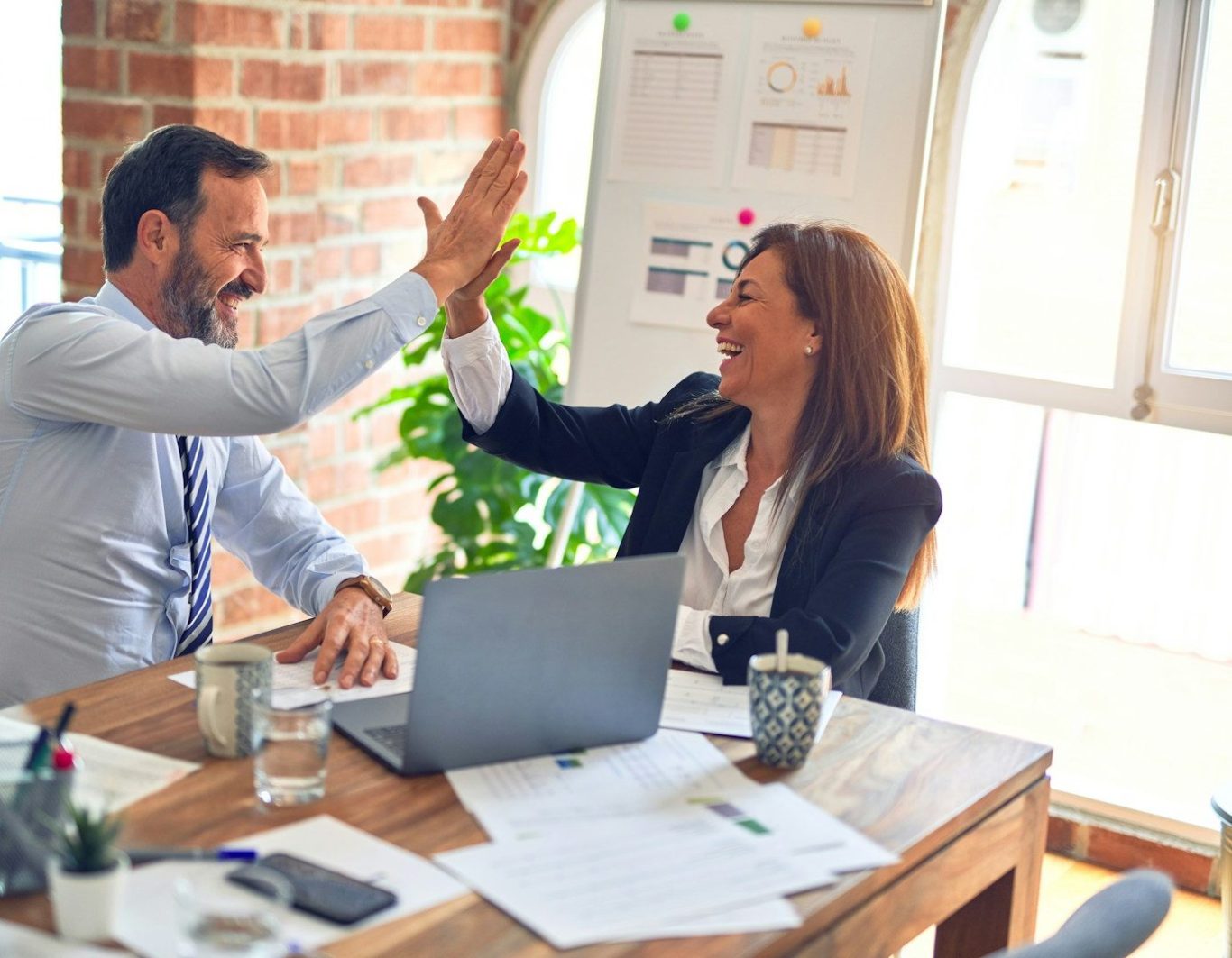 Dos profesionales sonrientes se dan un "high five" en una oficina luminosa.