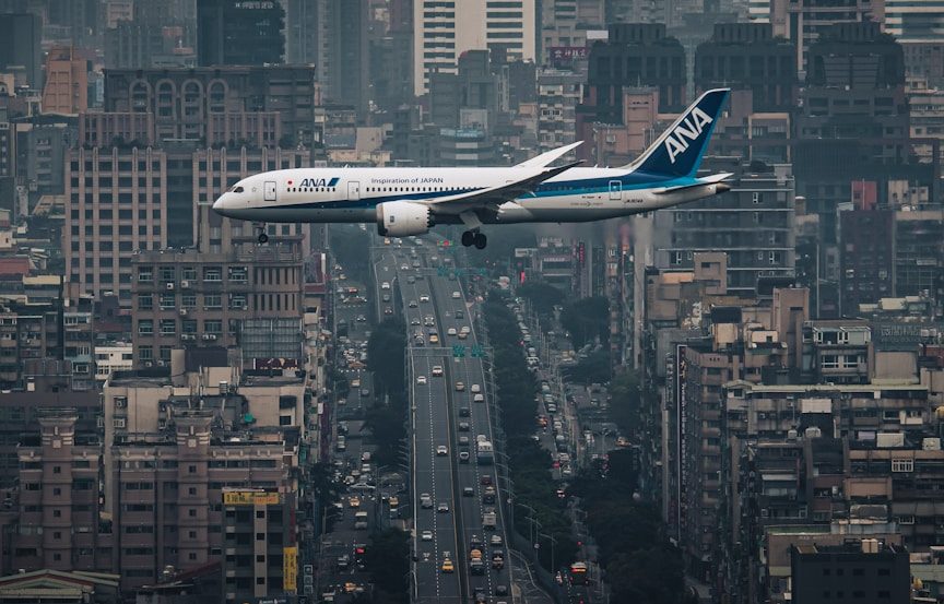 Un avión sobrevuela una ciudad densa, entre edificios y una atmósfera brumosa.
