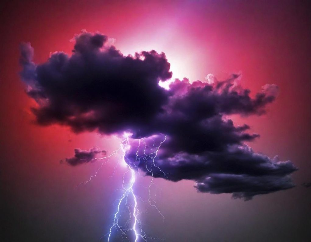 Nube oscura iluminada por un rayo en un cielo de tonos púrpuras y rojizos.