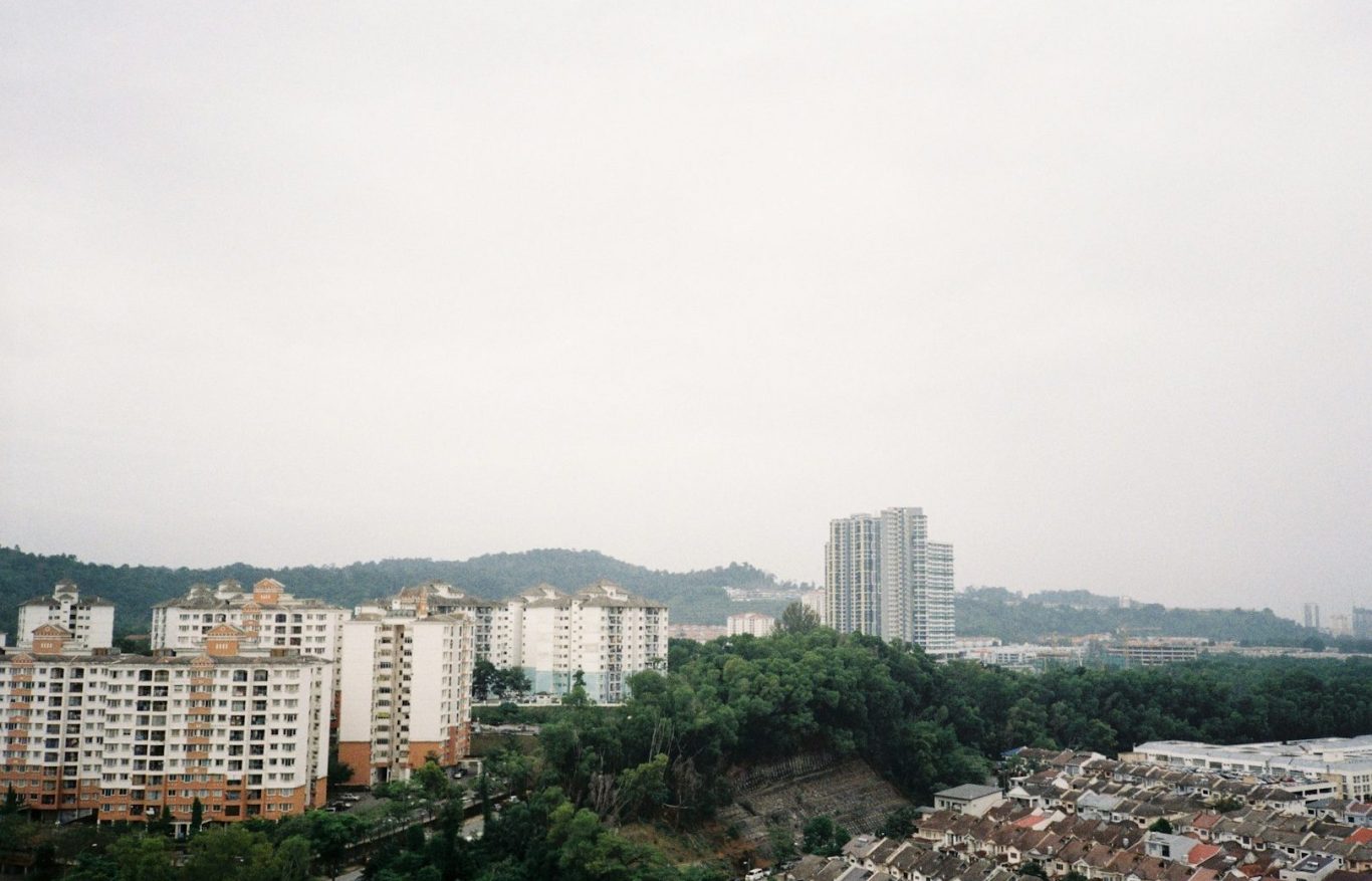 Vista de edificios urbanos con montañas y un cielo nublado en el fondo.