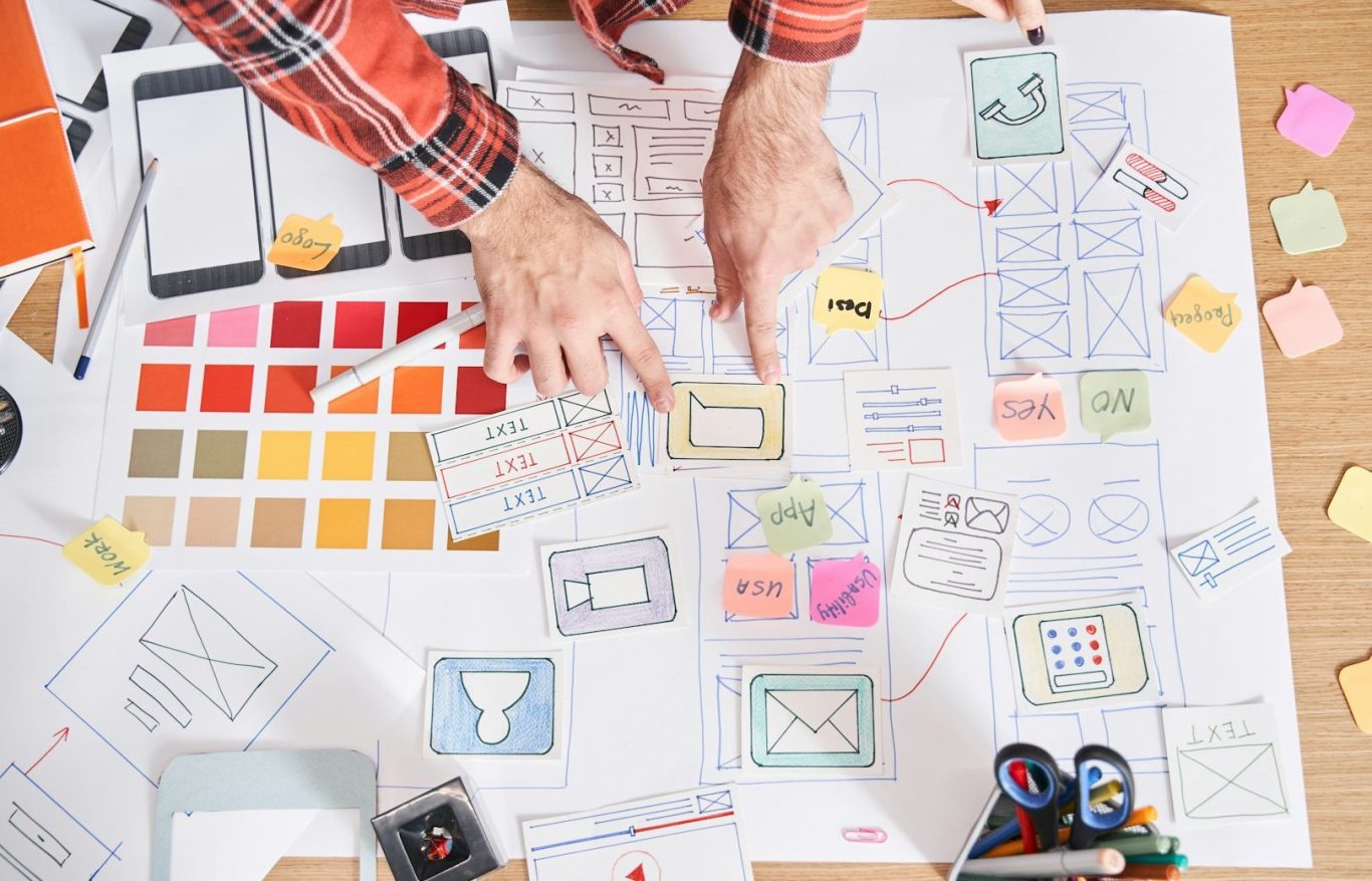 Manos sobre una mesa con bocetos, notas adhesivas y paletas de colores.