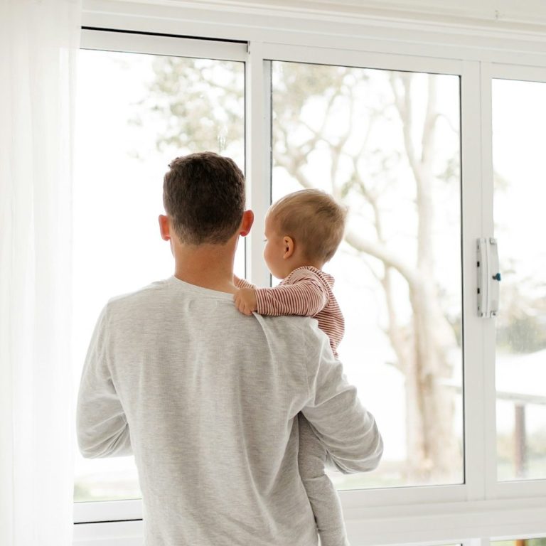 Padre e hijo Hombre sostiene a un bebé mientras miran por una ventana hacia un paisaje exterior.