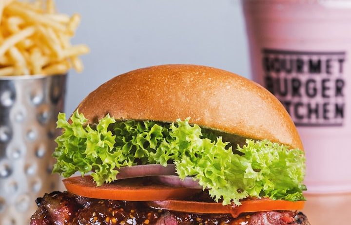 Hamburguesa con lechuga, tomate y cebolla, acompañada de papas fritas y un batido.