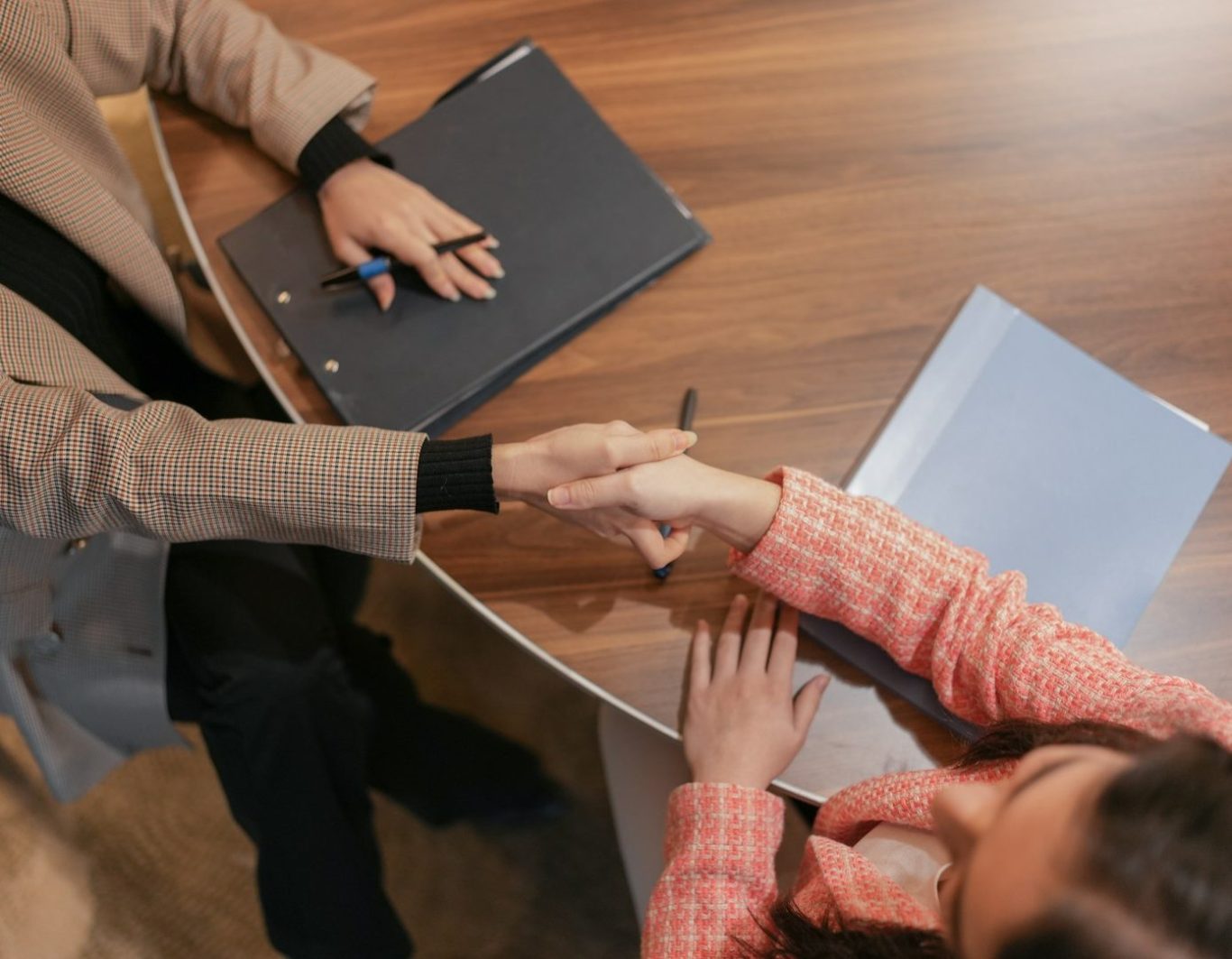 Dos personas se dan la mano sobre una mesa de trabajo. Una sostiene un bolígrafo.