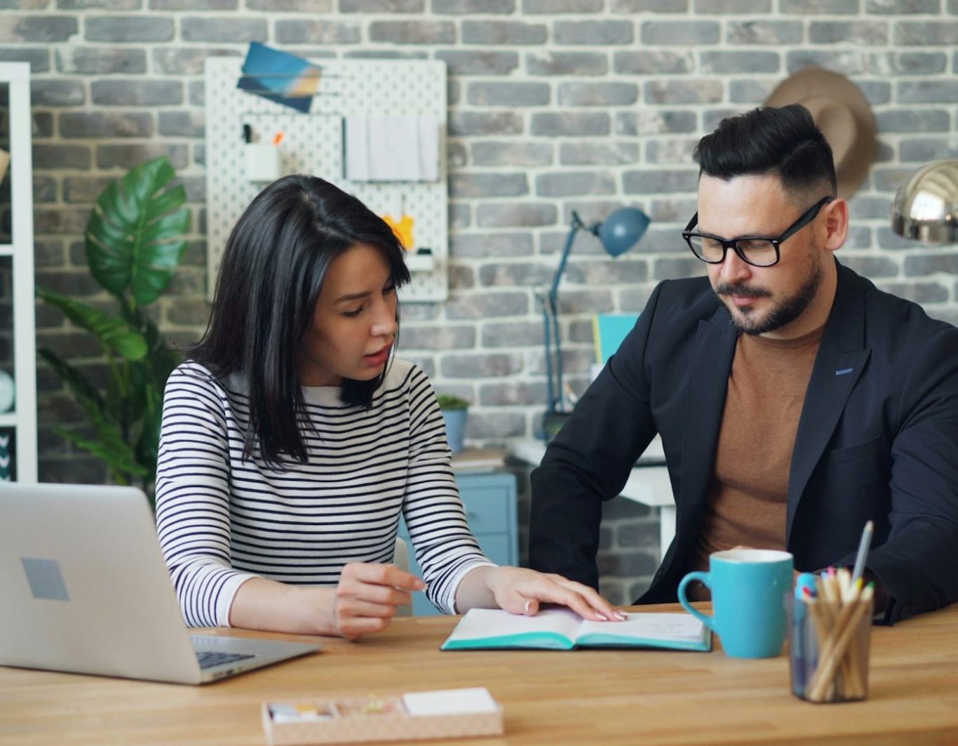 Dos personas colaboran en un proyecto, revisando documentos en una mesa de trabajo.