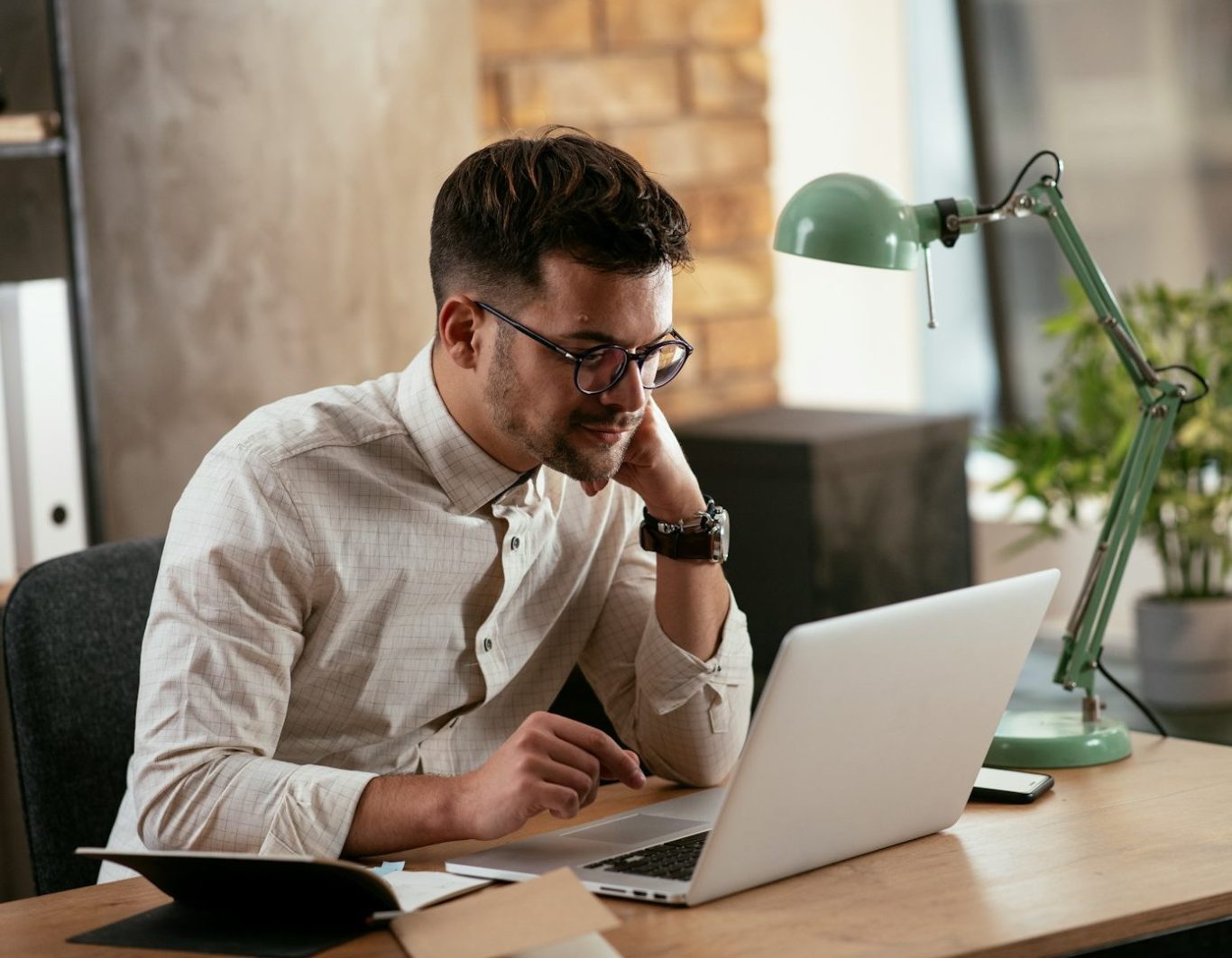 Hombre con gafas trabajando en un ordenador portátil en un entorno de oficina.