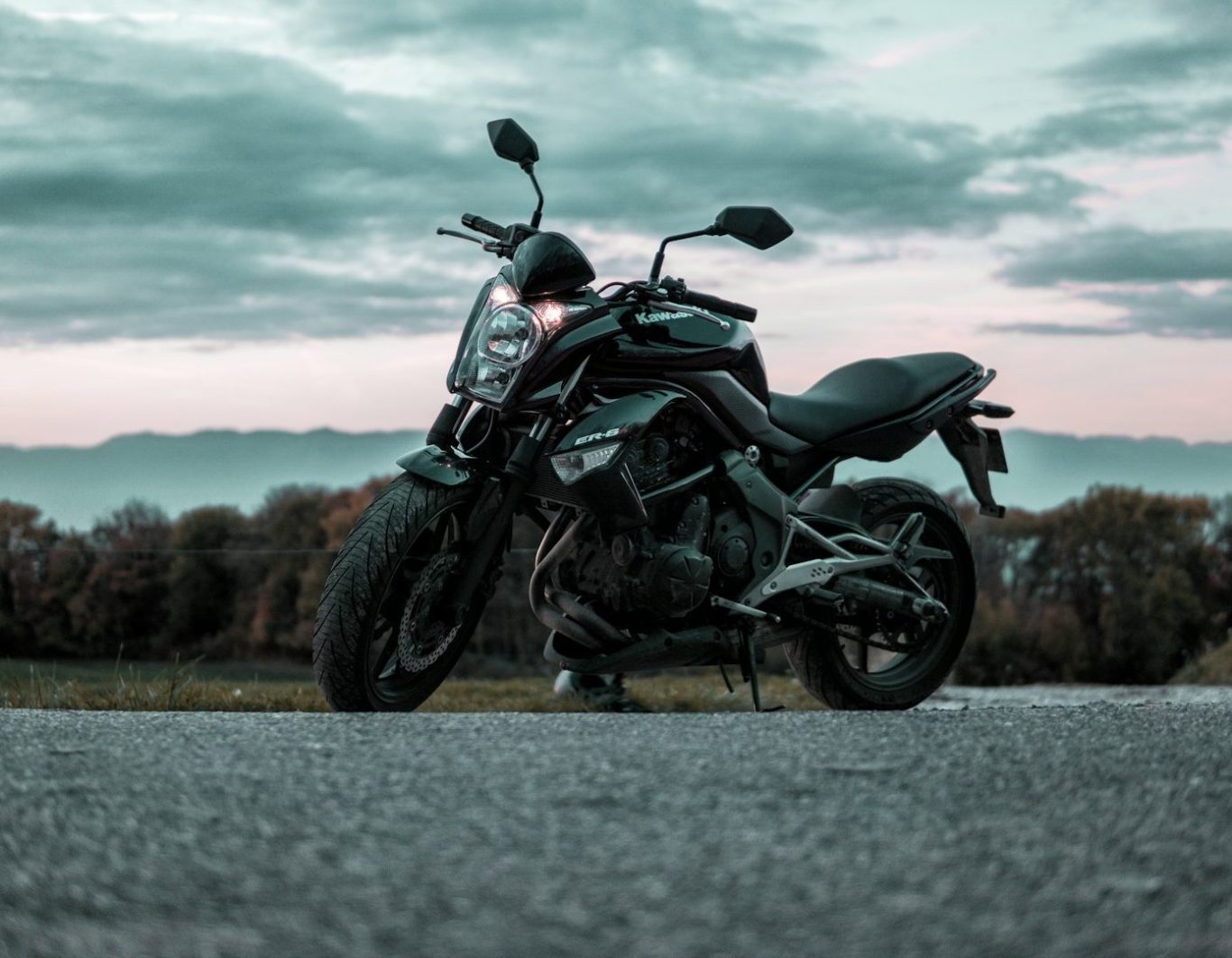 Motocicleta negra en una carretera con cielo nublado y paisaje al fondo.