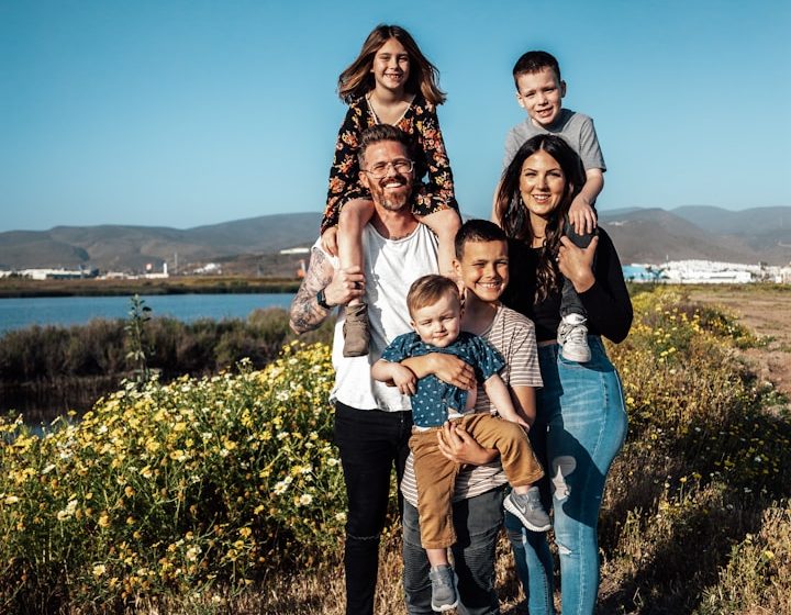 Familia sonriente en un campo, con niños sobre los hombros de los adultos.