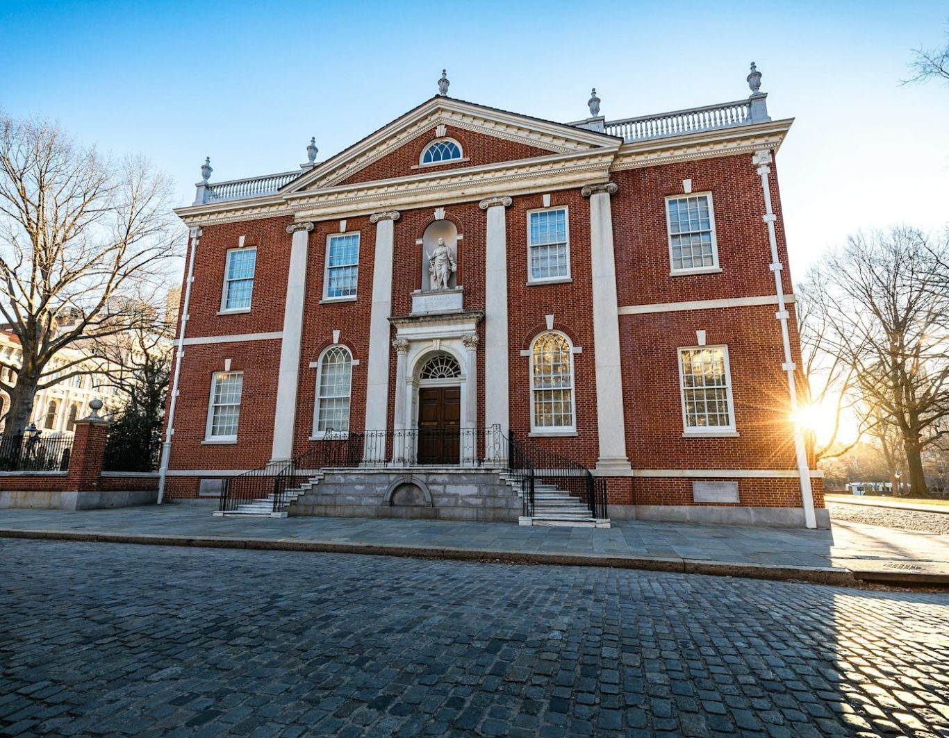 Edificio histórico de ladrillo rojo con columnas y un sol saliendo detrás.