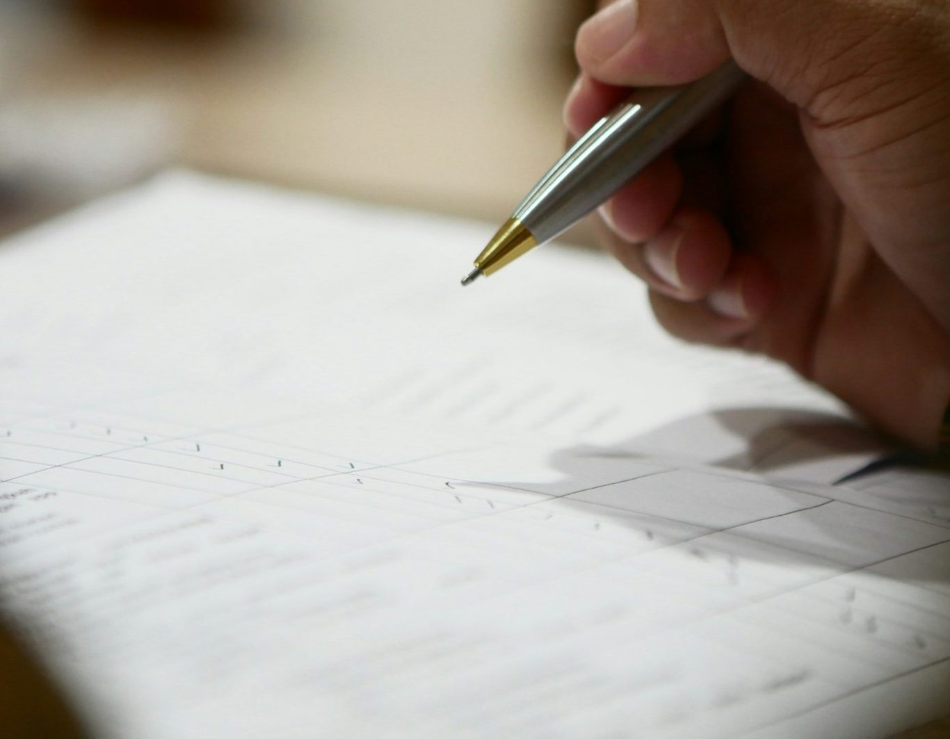 Mano sosteniendo un bolígrafo, escribiendo sobre una hoja de papel.