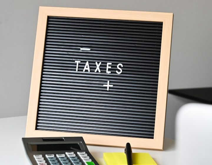 Calculadora, gafas, post-it y un cartel que dice "TAXES" en un entorno de oficina.