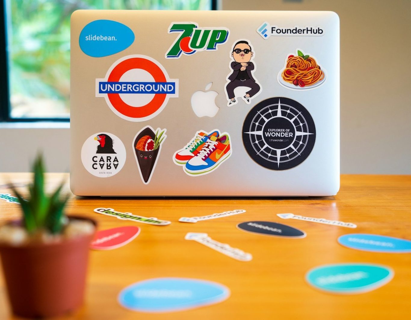 Portátil decorado con pegatinas coloridas sobre una mesa de madera y una planta pequeña.