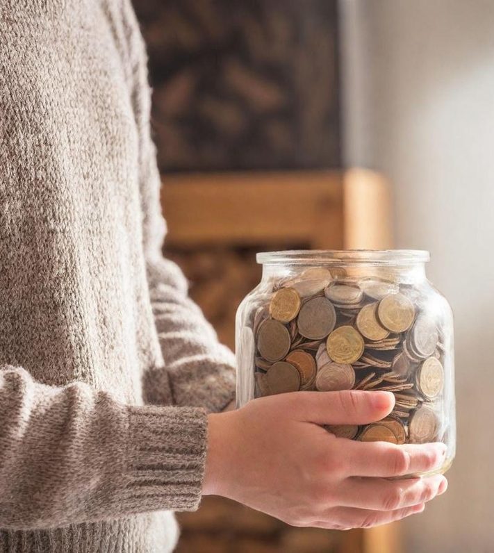 Una persona sostiene un tarro de cristal lleno de monedas.