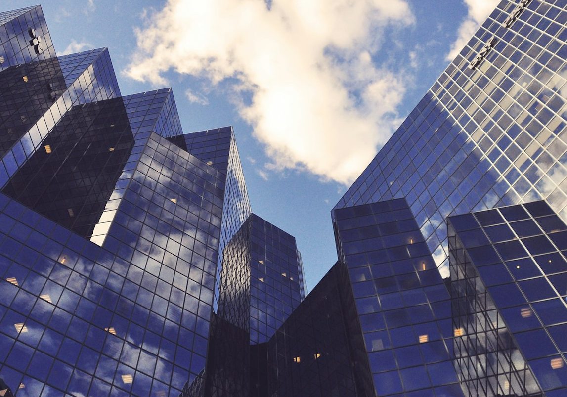 Rascacielos de vidrio reflejando el cielo con nubes en un entorno urbano.