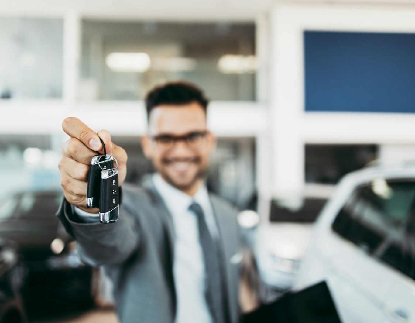 Hombre sonriente en traje, sosteniendo una llave de coche en un concesionario.