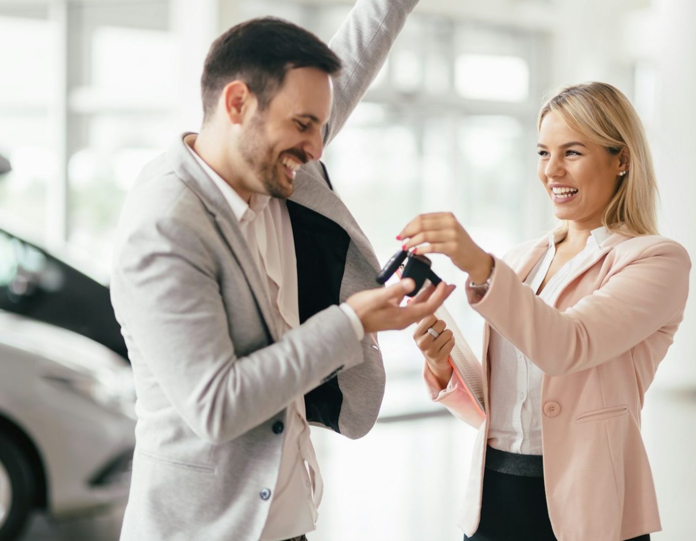 Hombre sonriente recibe una llave de coche de una mujer en un concesionario.