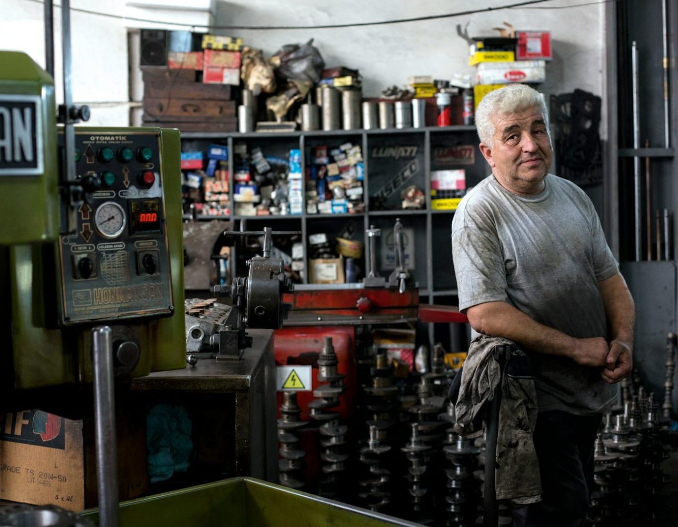 Hombre sonriente en un taller, rodeado de herramientas y piezas mecánicas.