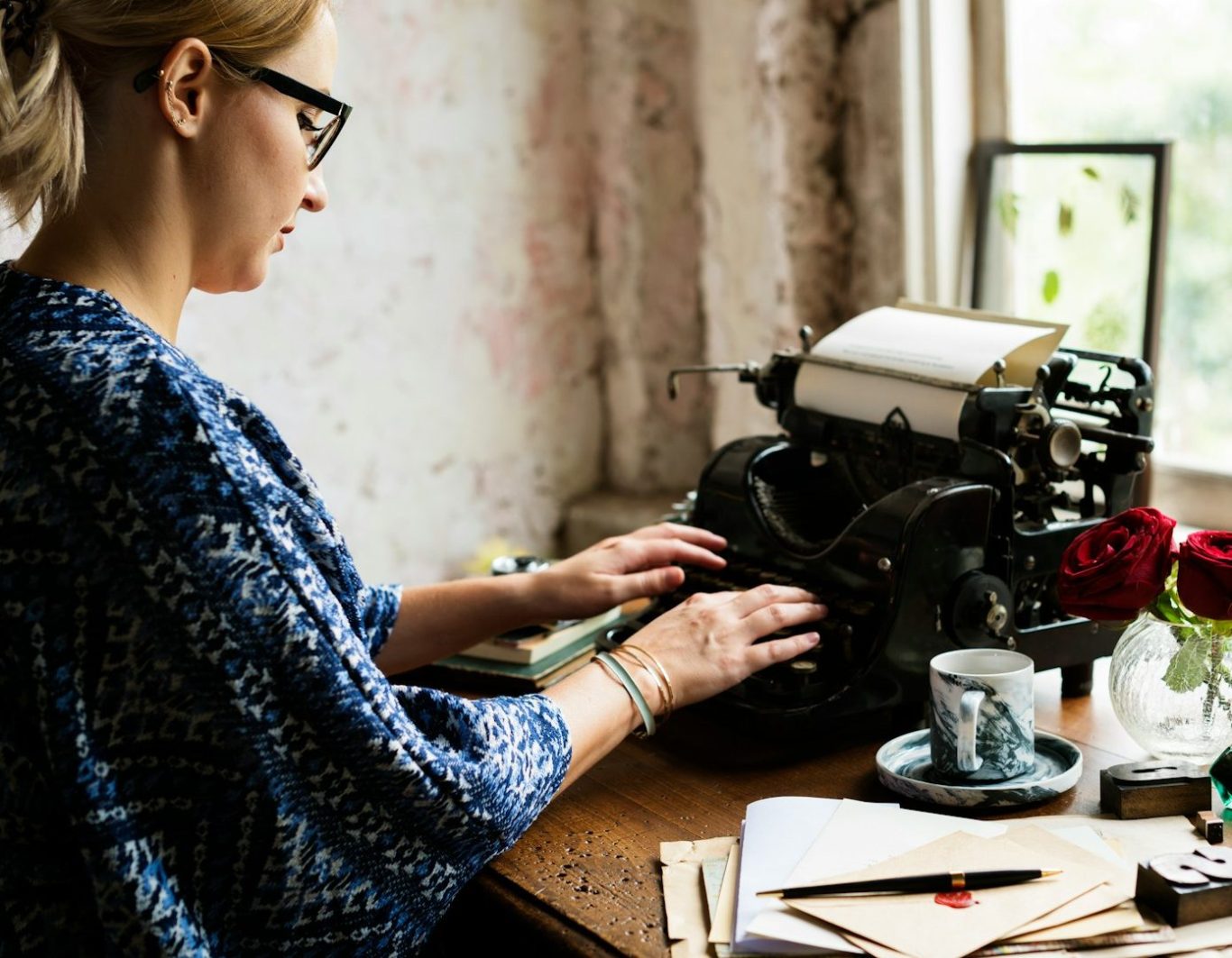 Mujer escribiendo en una máquina de escribir vintage, con flores y una taza de café cerca.