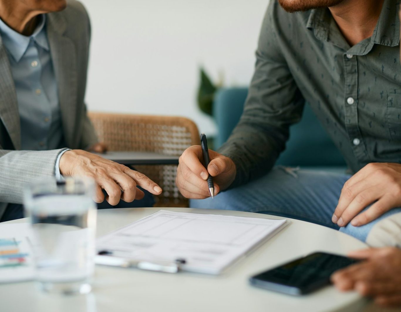 Dos personas revisan documentos sobre una mesa, una sostiene un bolígrafo.