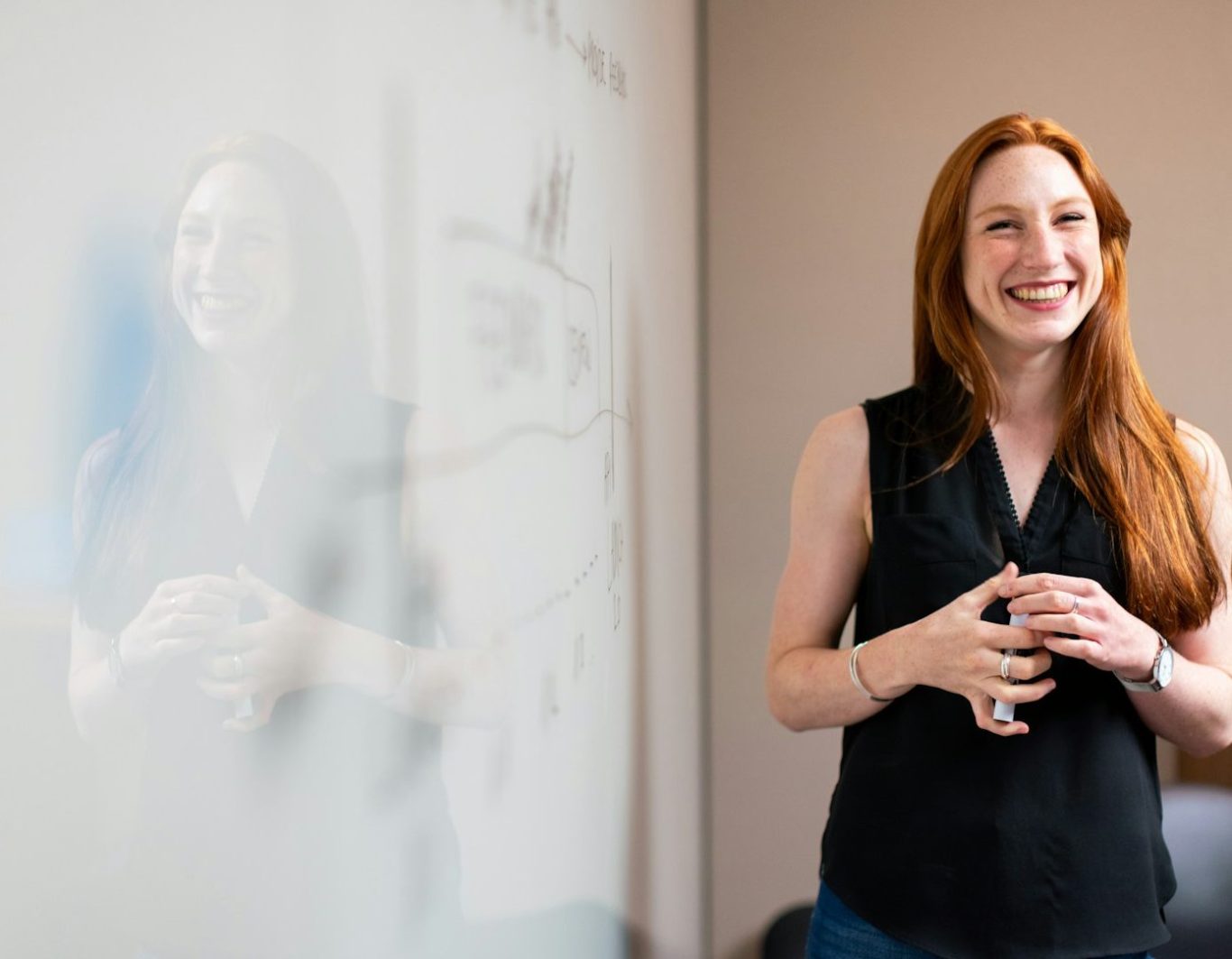 Mujer sonriente con cabello largo y rojizo, de pie frente a una pizarra blanca.